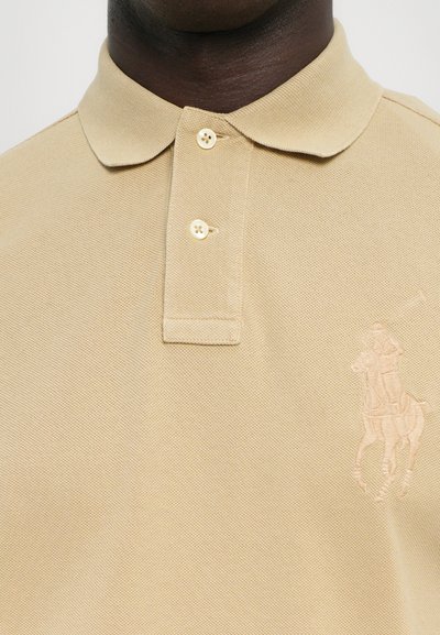 Bežs kokvilnas polo krekls ar teksturētu rakstu, divu pogu aizdari un izšūtu jātnieka logotipu kreisajā pusē.