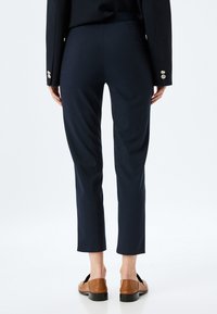 Marineblauwe broek met een getailleerde pasvorm, een cropped lengte en een gladde textuur. Voorzien van een verborgen tailleband en subtiele stikseldetails.