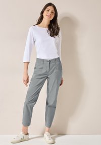 Grå, smala byxor med elastisk midja och sidofickor, kombinerat med en vit långärmad topp och ljusa sneakers.
