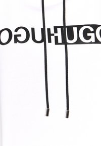Felpa bianca con un audace logo nero "HUGO". Caratterizzata da nastri neri con punte metalliche, realizzata in tessuto morbido.