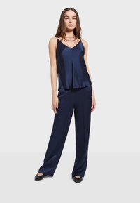 Navy jedwabna koszulka na ramiączkach z dekoltem w serek, zestawiona z luźnymi, granatowymi spodniami, charakteryzującymi się gładką fakturą i swobodnym krojem.