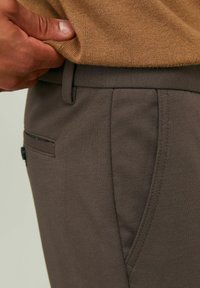 Pantalones de tela marrón con una textura suave, que cuentan con bolsillos laterales y traseros. Vista en primer plano de la cinturilla y los detalles de los bolsillos.