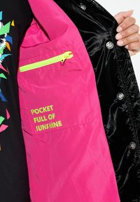 Tasca interna rosa con zip e il testo "POCKET FULL OF SUNSHINE" in giallo brillante. Tessuto esterno in satin nero.