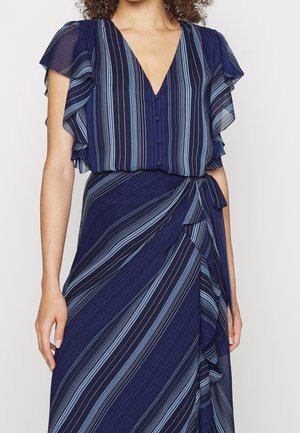 Mujer que lleva un vestido azul marino a rayas con mangas acampanadas, botones forrados de tela y un detalle de lazada lateral en la cintura.