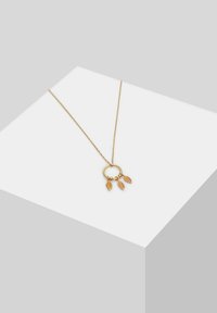 Collana color oro con un pendente circolare che presenta tre ciondoli a forma di foglia. La catena è delicata e mostra dettagli intricati sulle foglie.