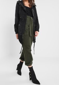 Czarna lekka kurtka z kapturem, z zamkiem błyskawicznym i detalami ze sznurkiem. Oliwkowe spodnie cargo z paskiem w talii i zwężanymi mankietami. Czarne botki na obcasie.