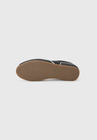 Black shoe sole with a textured surface, rounded toe, and beige rubber outsole. Features a minimalist design with a smooth black upper.