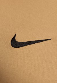 Logo Swoosh Nike noir brodé sur un tissu beige texturé, mettant en valeur l'emblème de la marque sur le matériau de vêtement.