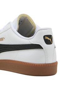 Fehér sneaker szintetikus bőrből, fekete csíkkal, gumitalppal és arany logó díszítéssel a saroknál és az oldalon.