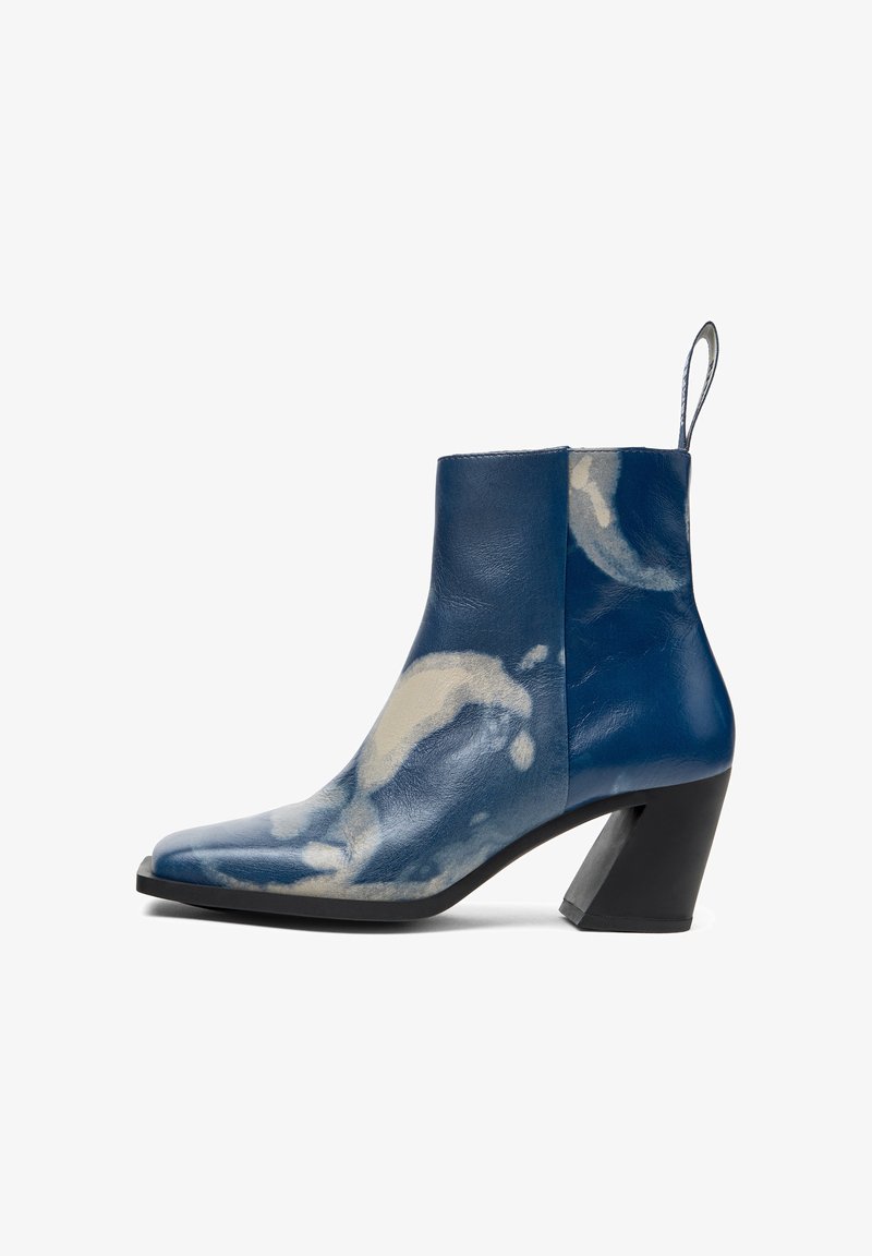 Bottes de cheville en cuir bleu avec un talon pointu, présentant un motif blanc en forme de nuage et un talon noir épais. Onglet en boucle pour un enfilage facile.