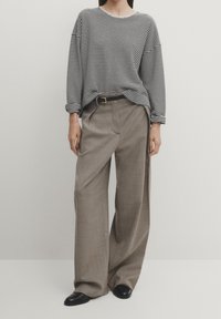 Maglione leggero a righe in bianco e nero; abbinato a pantaloni larghi grigi chiari con cintura e texture sottile. Scarpe nere.