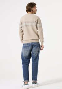 Beige gestrickter Pullover mit horizontalen Streifen, kombiniert mit hellblauen Jeans. Weiße Sneaker mit grünen Akzenten. Lässiger, lockerer Schnitt.