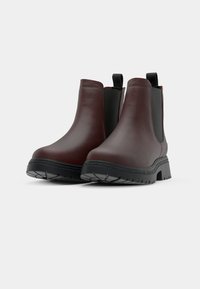 Bruna läderankelboots med svarta elastiska sidopaneler, texturerad gummisula, rund tå och öglade dragflikar bak.