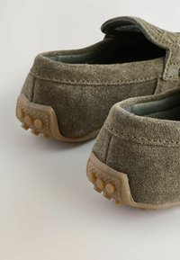 Les chaussures slip-on en daim vert présentent un petit talon, un bout rond et une semelle extérieure en caoutchouc texturé avec de petits renflements pour une traction et une durabilité accrues.