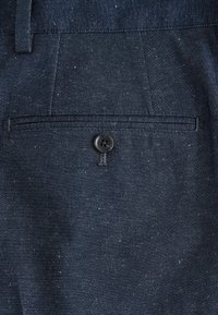 Tmavomodré denimové nohavice so zadným vreckom, ktoré je uzatvárateľné na gombík, s pútkami na opasok viditeľnými v hornej časti.