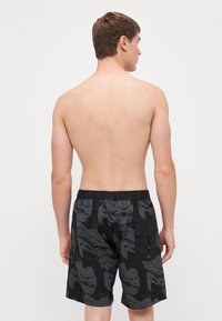 Shorts de bain noirs avec un motif texturé et une taille élastique, disposant d'une poche latérale pour le rangement. Vue de dos.