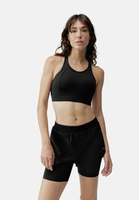 Melna sporta krūšturis ar sporta aizmuguri, savienots ar melniem sporta šortiem. Materiāli ir viendabīgi un elastīgi, ar elastīgu jostu.