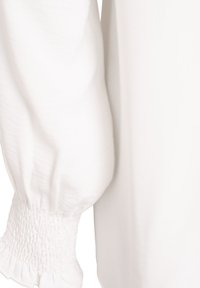 Manga blanca larga con puño recogido y elástico y detalle de volantes en tela ligera.