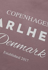 Poros rózsaszín pamutszövet fehér felirattal: "COPENHAGEN", "PARLHER", "Denmark" és "Established 2017". Sima textúra, laza dizájn.