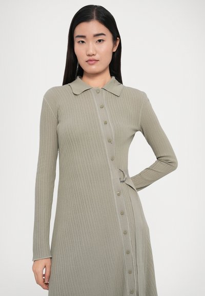 Robe à manches longues côtelée en vert doux avec un devant boutonné, un col et un détail anneau métallique à la taille. Texture de tissu lisse.