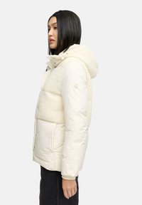 Donsjack in off-white, met een pluizige schapenvacht bovenkant, capuchon en zijzakken, met een gladde onderkant en ritssluiting.