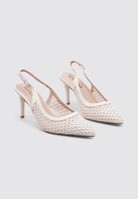 Tacones slingback de malla blanca con puntas afiladas, tiras estrechas y un tacón de aguja de 3 pulgadas. Diseño texturizado con un borde suave.