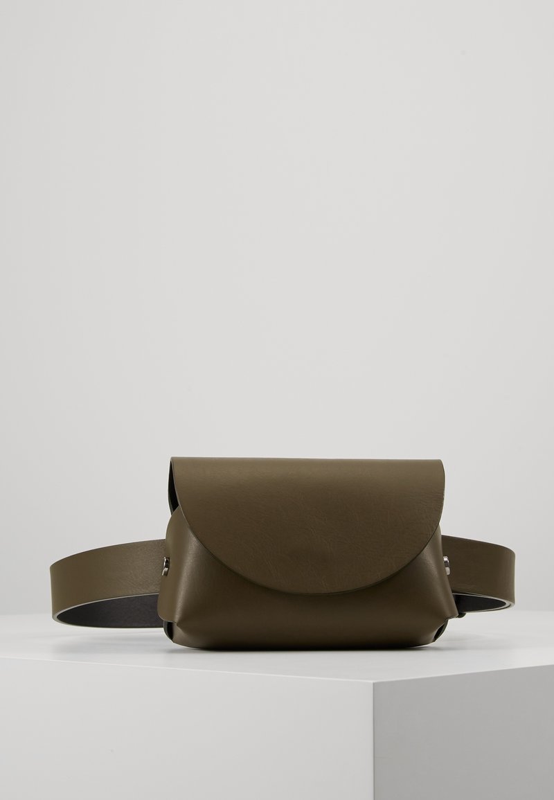 Sac ceinture en cuir vert olive foncé avec une fermeture à rabat incurvée, présenté sur une surface blanche sur un fond gris clair uni.