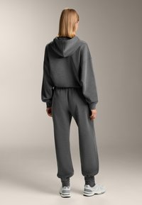 Hanorac gri și pantaloni jogger asortați din țesătură moale, cu croială lejeră, manșete elastice și glugă. Asortate cu adidași gri deschis.