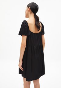 Černé šaty s krátkými nafouklými rukávy, otevřenými zády a nařaseným živůtkem. Vyrobené z měkké látky, mají volný střih a délku nad kolena.