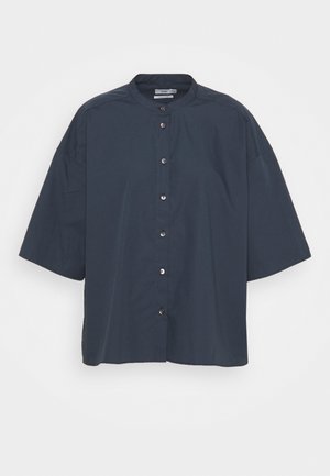 Chemise bleu foncé à manches courtes avec boutons, col rond et coupe ample, présentée sur un fond clair uni.