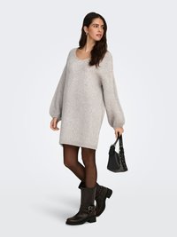 Gray knitted oversized sweater dress with long sleeves, paired with dark brown knee-high boots and a small black handbag.