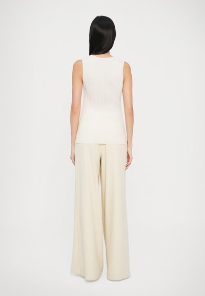 Kerman ribbattu astuvan toppi yhdistettyinä leveälahkeisiin kermanvärisiin housuihin. Silkkinen pinta ja muotoiltu siluetti, joka esittelee minimalistista muotoilua.