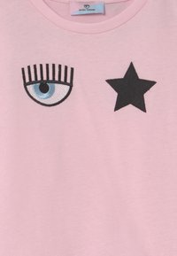 Maglietta in cotone rosa chiaro con ricami di un occhio blu e stelle nere. Scollo rotondo e tessuto morbido.