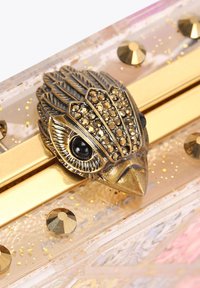 Clutch in acrilico traslucido con chiusura a forma di uccello in tonalità oro, decorata con dettagli in rhinestone e glitter dorati. Texture liscia.