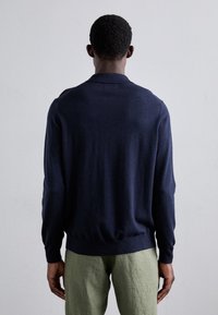 Marinblå stickad tröja med krage, lång ärm och ribbade muddar. Tyget verkar mjukt och slätt, med en kroppsnära passform.