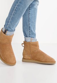 Bottines en suède beige à bout rond, semelle plate et détail de coutures contrastantes ; portées avec un jean bleu retroussé.