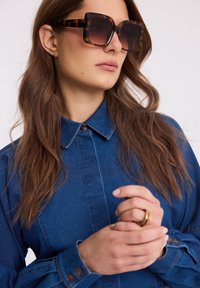 Kwadratowe okulary przeciwsłoneczne w wzór żółwia z gradientowymi soczewkami, zestawione z dżinsową koszulą z zapięciem na guziki i długimi rękawami.