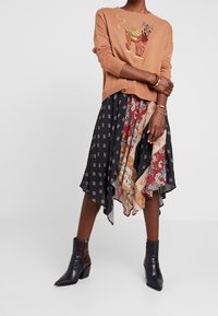 Pull couleur rouille avec broderie de tigre, associé à une jupe noire asymétrique à motifs multiples et des bottines noires brillantes.