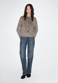 Beige leopard print jacket with a collared neckline and black buttons, paired with blue straight-leg jeans and black ankle boots.