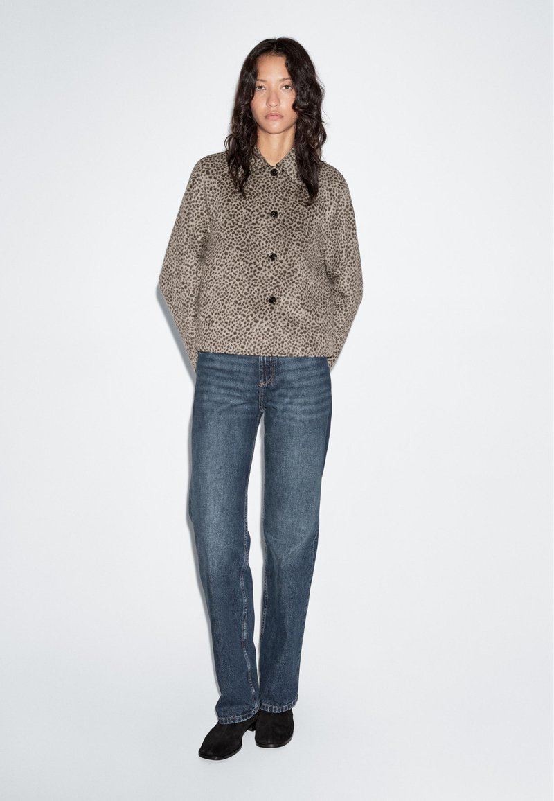 Beige leopard print jacket with a collared neckline and black buttons, paired with blue straight-leg jeans and black ankle boots.