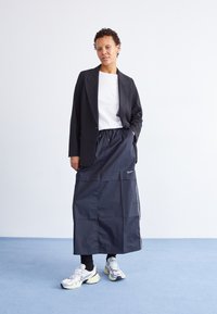 Black tailored blazer over a white t-shirt, paired with a navy skirt featuring an elastic waistband and side stripes. Silver sneakers complete the look.