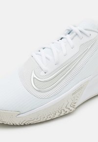Chaussure de sport blanche avec une semelle texturée, un logo Nike argenté en forme de virgule et le texte "PRECISION 7" sur le côté près de la semelle.