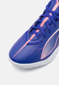Zapatilla deportiva azul con acentos en rosa, parte superior texturizada, diseño elegante y un detalle reflectante prominente en el lateral, con suela blanca.