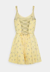 Gul blommig jumpsuit med justerbara axelremmar, korset design på baksidan och dragsko i midjan. Har små vita blommor och gröna blad.