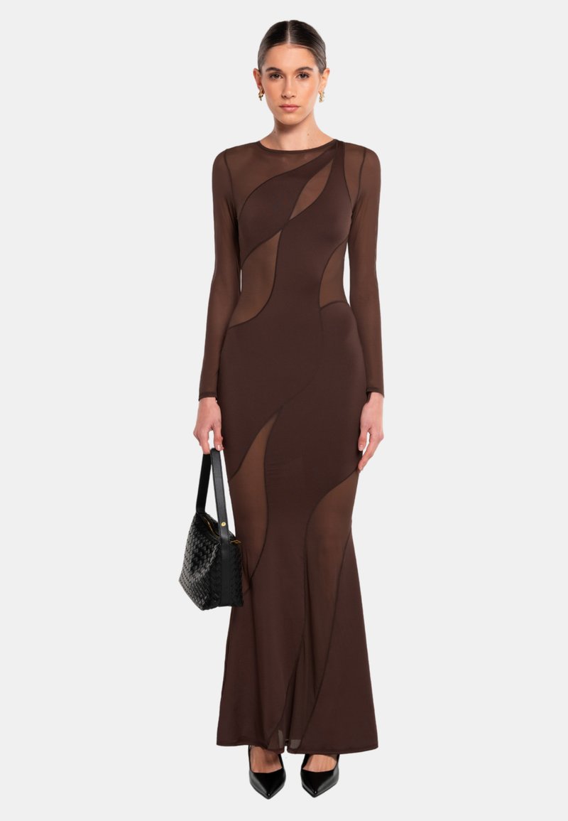 Langes braunes Kleid mit transparenten Einsätzen und langen Ärmeln. Hat eine taillierte Silhouette, abstrakte Ausschnitte und eine glatte Textur. Kombiniert mit einer schwarzen Handtasche.