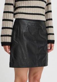 Falda mini de cuero negra con una textura suave, que presenta una silueta ajustada y costuras en ángulo. Combinada con un suéter de punto a rayas.