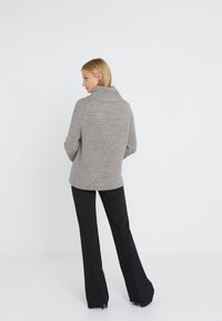 Gestrickter grauer Pullover mit Stehkragen, gerippter Textur und lässiger Passform, kombiniert mit schwarzen maßgeschneiderten Hosen. Rückansicht gezeigt.