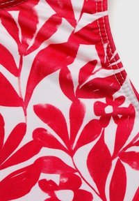Tissu floral rouge et blanc avec des motifs de feuilles, présentant une texture lisse et des couleurs vives, adapté pour des vêtements ou des accessoires.