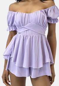 Vestido lila con hombros descubiertos, mangas abullonadas, cintura ceñida y falda en capas. Tela suave con textura ligera y fluida y un brillo sutil.