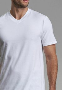 Weißes Baumwoll-T-Shirt mit V-Ausschnitt, kurzen Ärmeln, weichem Material und glatter Optik, ohne Logos oder Muster.